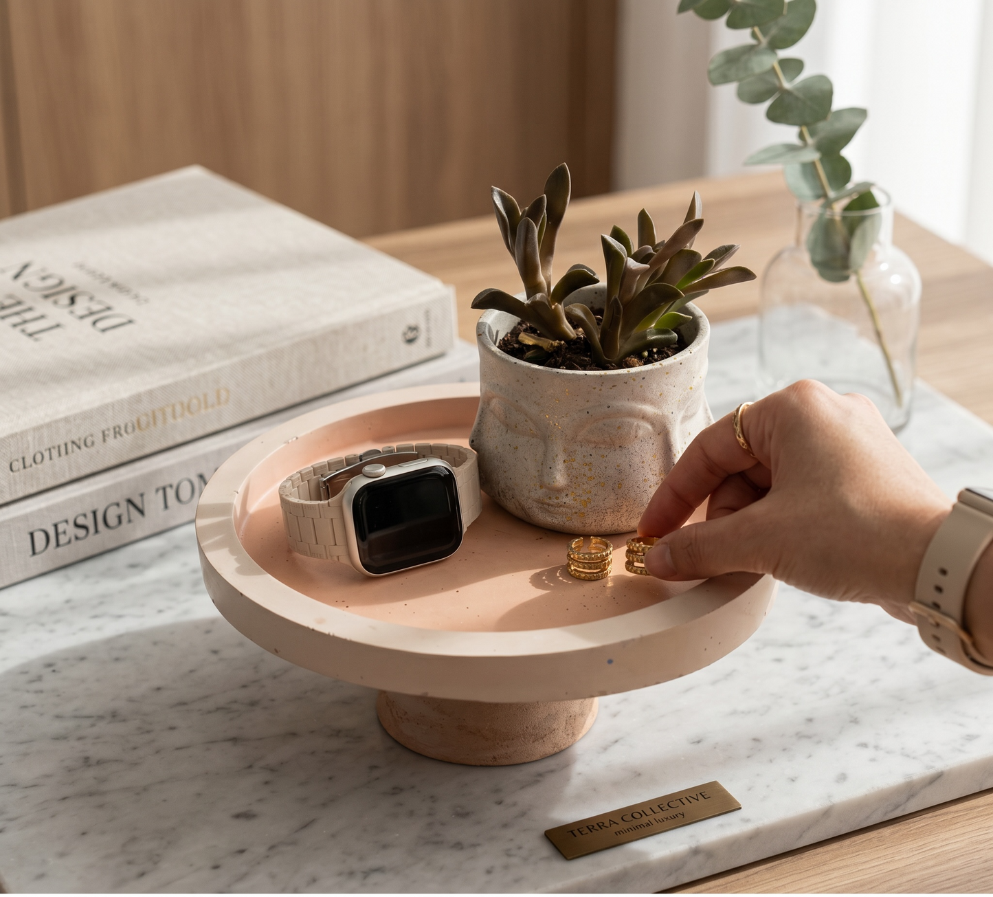 Person placing a ring on a small round wooden table with a plant and smartwatch.
