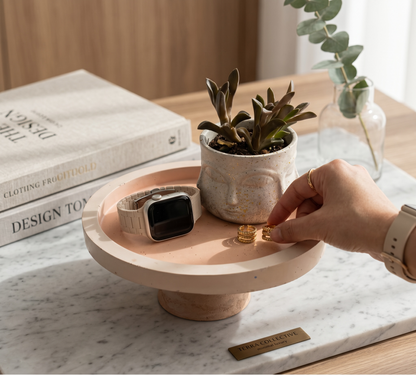 Person placing a ring on a small round wooden table with a plant and smartwatch.